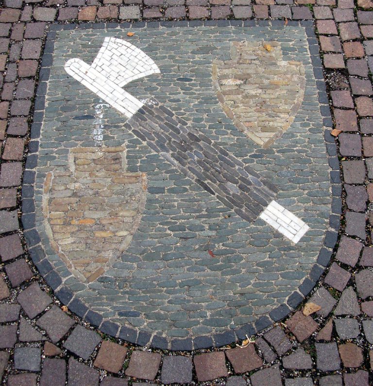 Das Bild zeigt ein kunstvolles Pflastermosaik im Ortsteil Zarten von Kirchzarten, das das Wappen des Ortsteils darstellt. Das Mosaik ist Teil der städtebaulichen Gestaltung und unterstreicht die lokale Identität und das Gemeinschaftsgefühl. ​