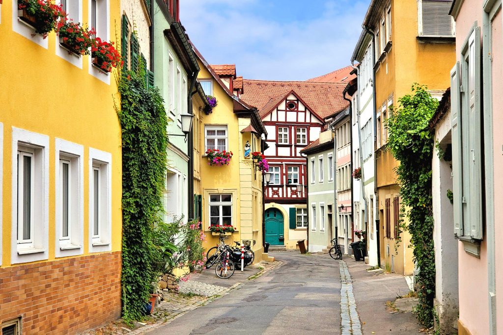 Bunte Häuser in einer ruhigen Straße - Das Bild zeigt einen pittoresken Straßenzug in Bamberg, wahrscheinlich aus dem historischen Sandgebiet mit engen Gassen, traditionellen Fachwerkhäusern und Palais unter Denkmalschutz. Es illustriert den UNESCO-Weltkulturerbe-Status der Bamberger Altstadt mit charakteristischen Bauepochen.