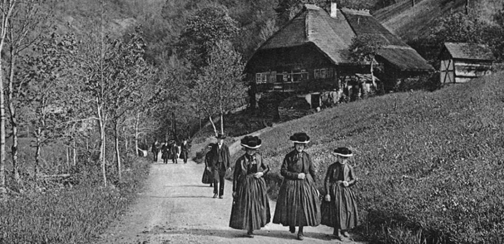 Frauen in traditionellen Kleidern spazieren - Das Bild zeigt den Bauwerk Talk im Schwarzwälder Freilichtmuseum Vogtsbauernhof, bei dem Experten und Interessierte über die Zukunft regionalen Bauens, Umnutzung und Sanierung historischer Gebäude diskutieren.